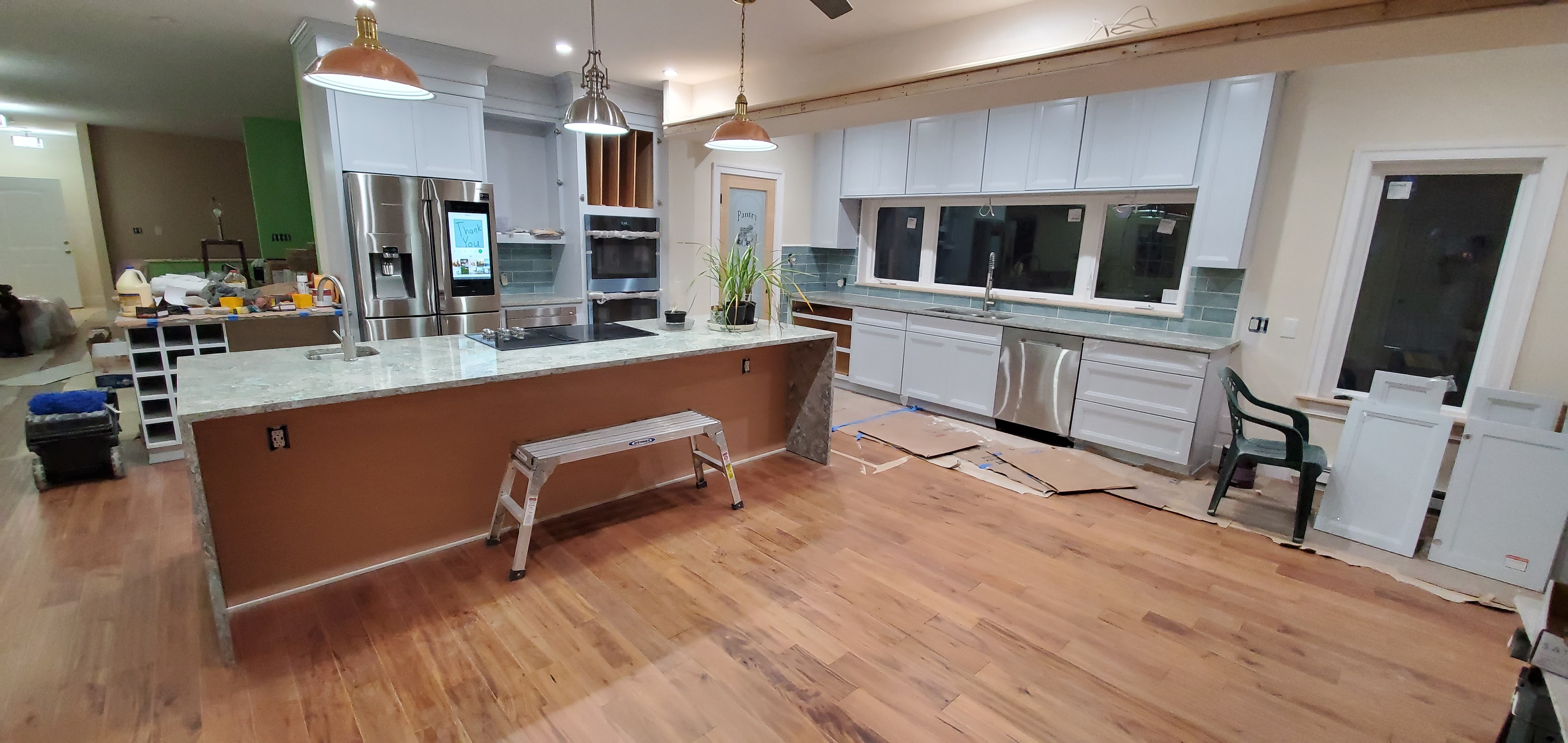 White kitchen renovation in progress with a large island, blue tile backsplash, and hardwood flooring